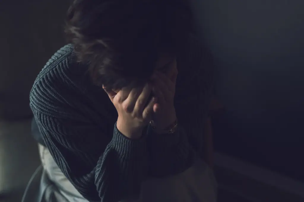 暗い部屋で頭を抱えて悩む女性